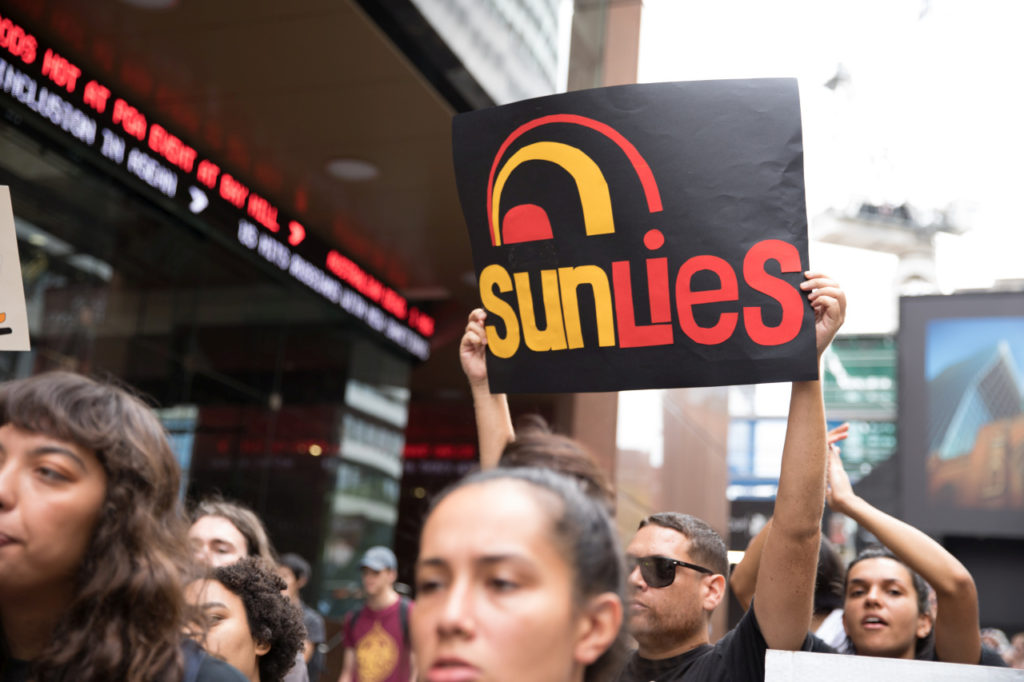 person holding placard saying "sun lies"