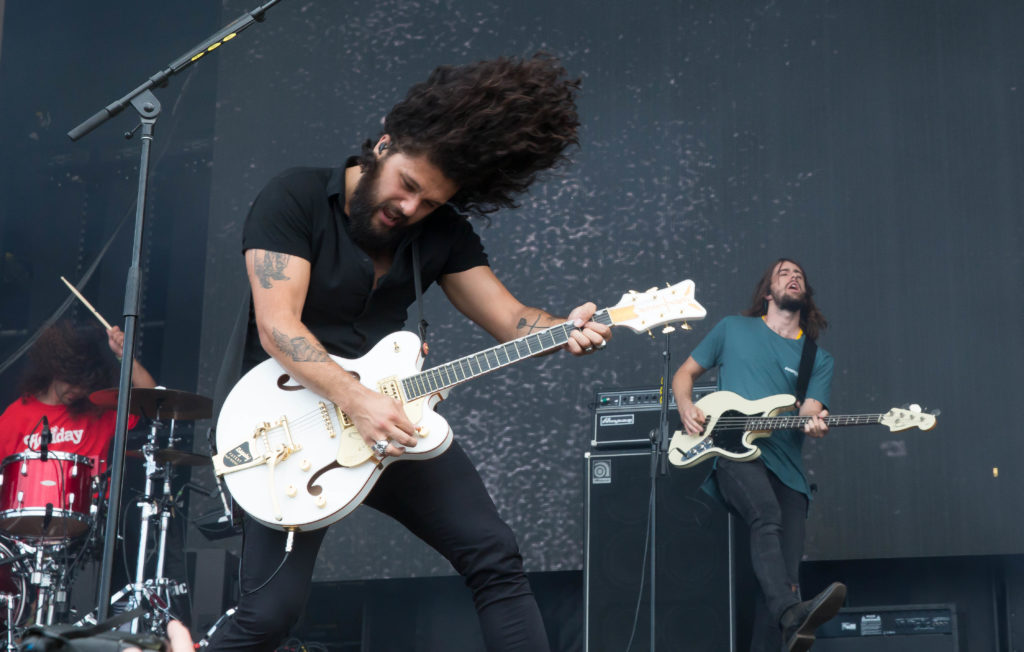 a band onstage with bearded guitarist rocking out, long curly hair flying