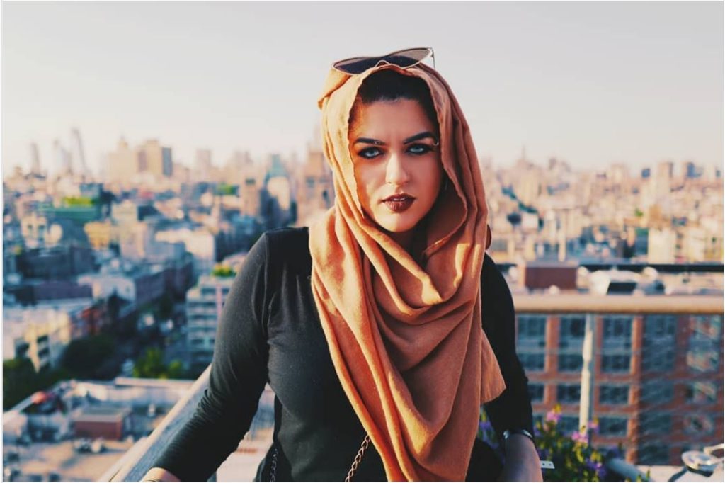 person with heavy eye makeup, wearing an orange hijab with sunglasses perched on top