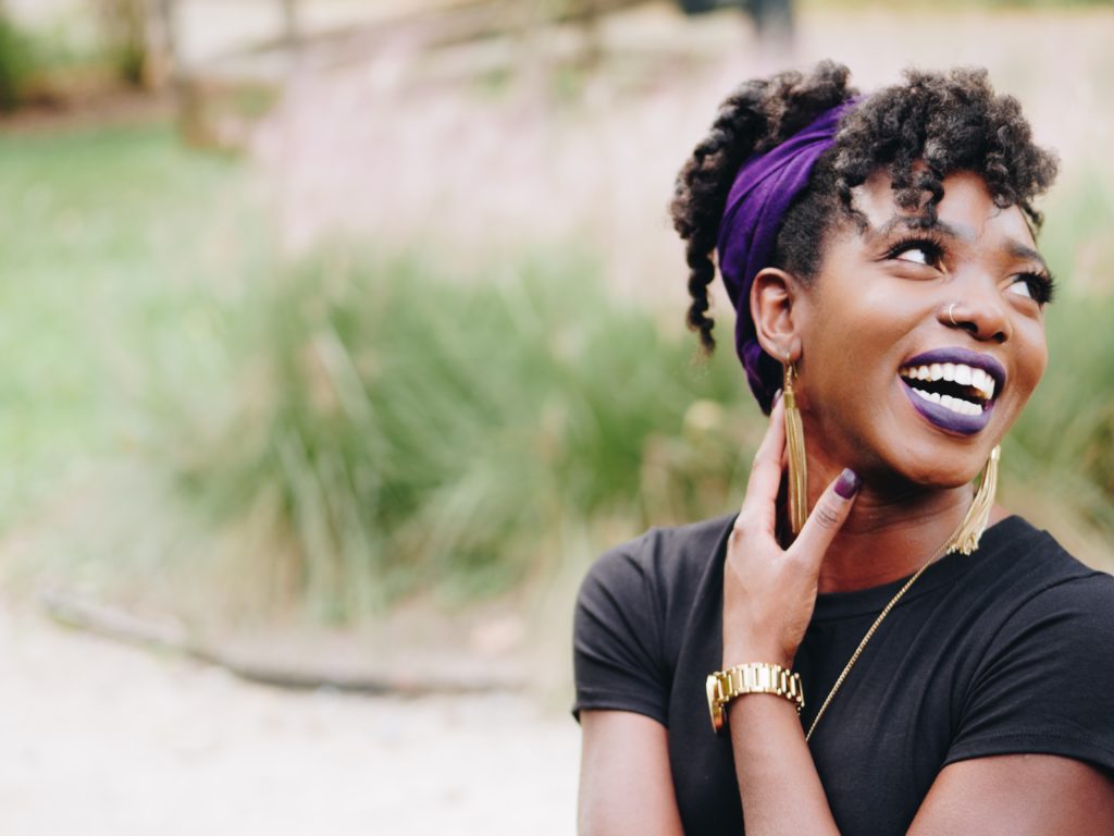 a black woman, laughing, with a purple headband and purple lipstick
