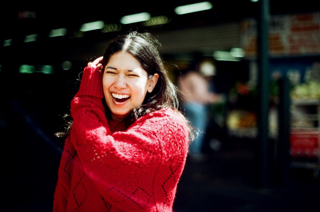 Gemma Mahadeo in a red jumper, smiling with closed eyes