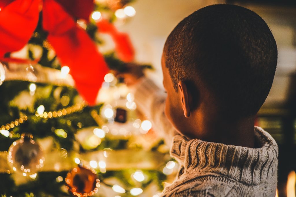 a short-haired black child facing a Christmas tree