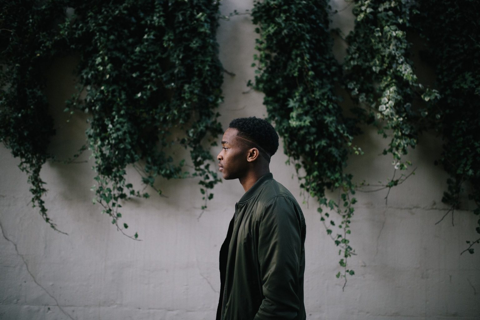 stock image of a black man in a green jacket, against a wall covered in vines