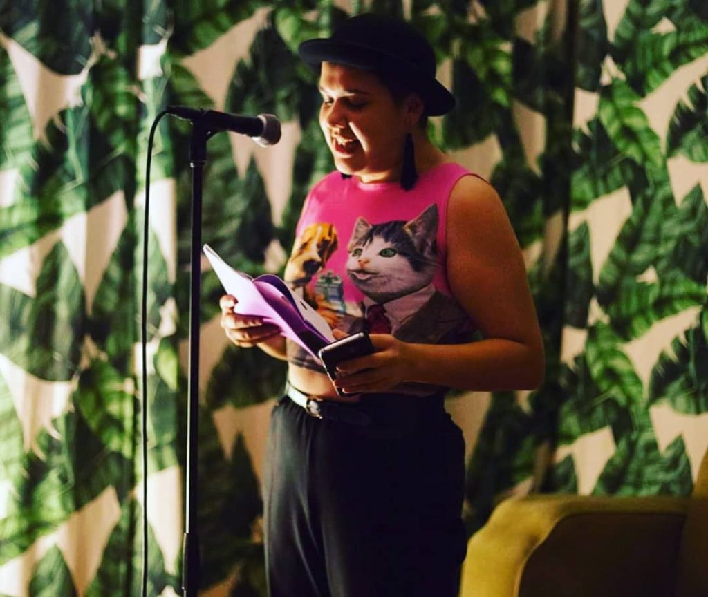 woman wearing pink crop top with cat and dog on it reading at a microphone