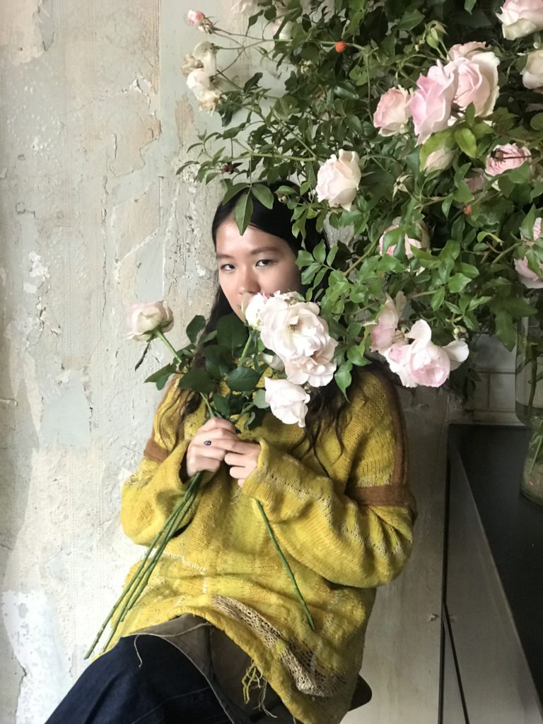 Photo of Panda Wong in a yellow jumper, half-obscured by flowers