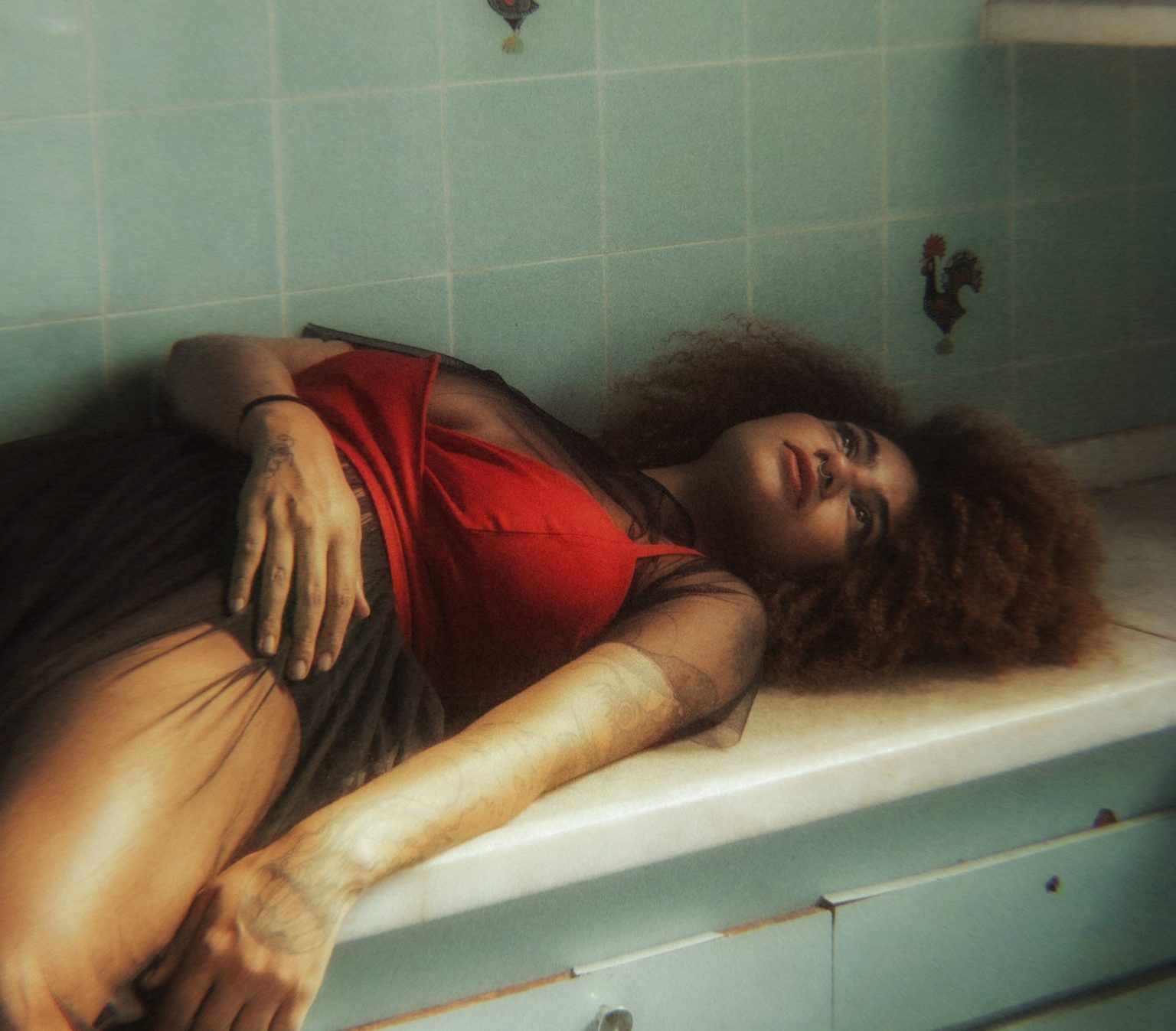 a model in a red top with a big afro lying on a bench