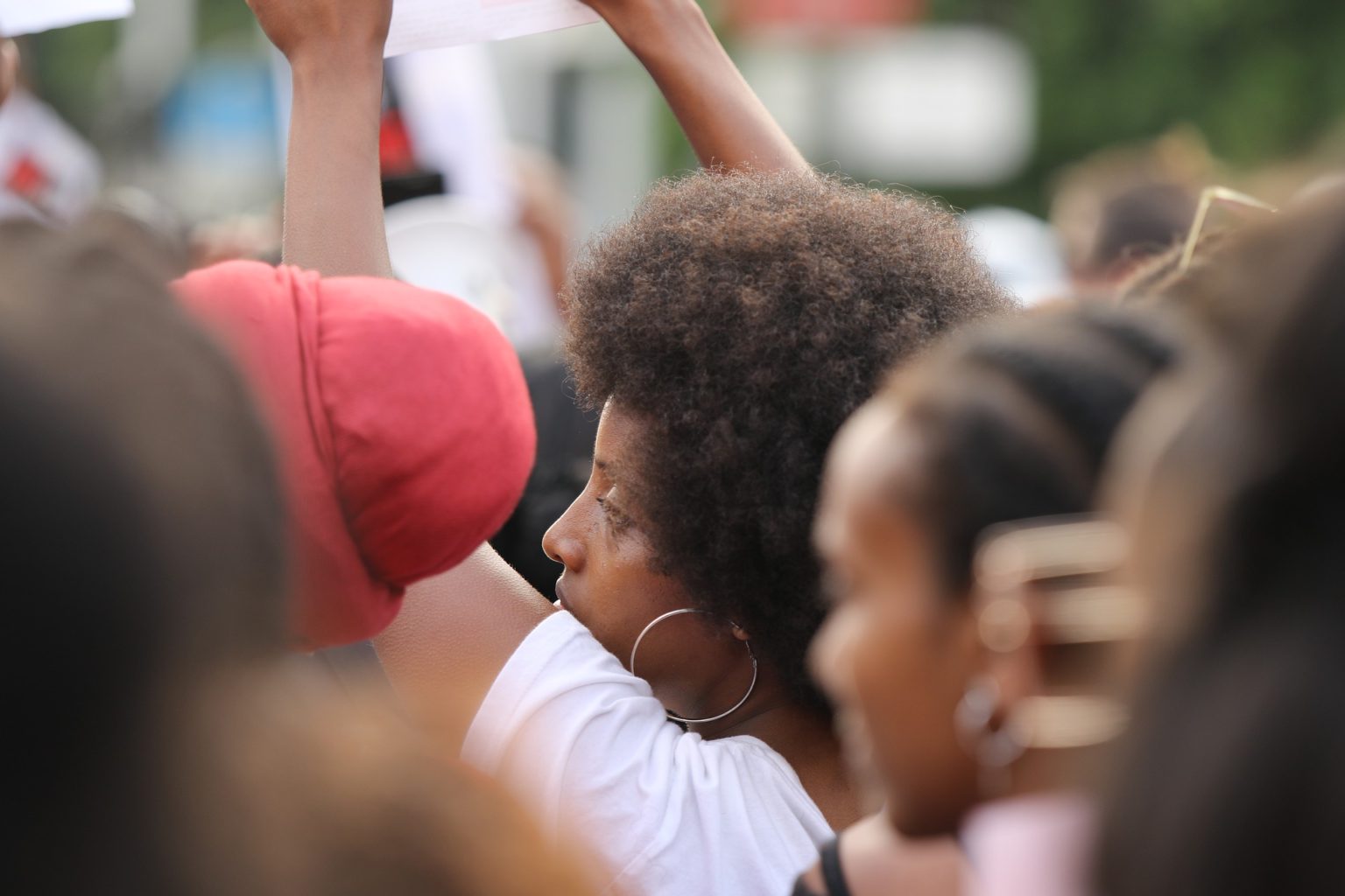 #blackllivesmatter - tired and frustrated looking black woman in a crowd of other black protesters at a rally, the woman's face is in side profile and she's holding up a protest sign not visible in the image