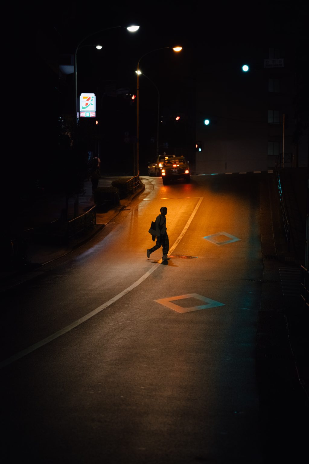 long shot of a lone person walking across a dimly lit street. The image is sombre and lonely.